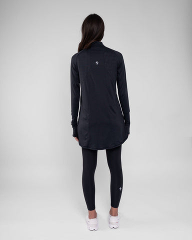 A model viewed from behind, wearing a dark long-sleeve ARMA shirt by Qynda with cooling fabric technology and black leggings, standing against a plain light background.